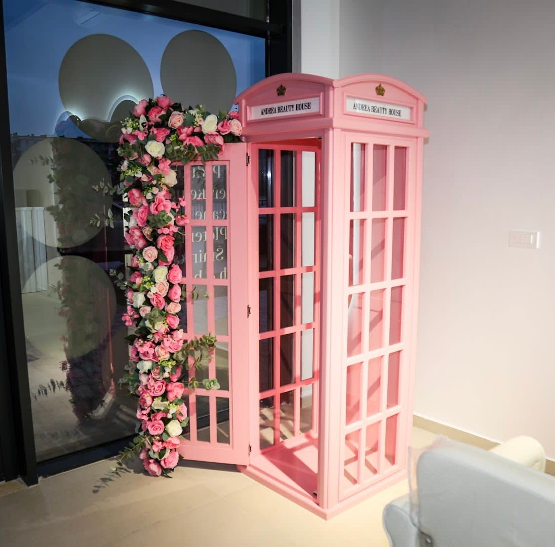 Roze telefonska govornica sa natpisom Andrea Beauty House, ukrašena vijencem od roza i bijelog cvijeća, u ulazu salona