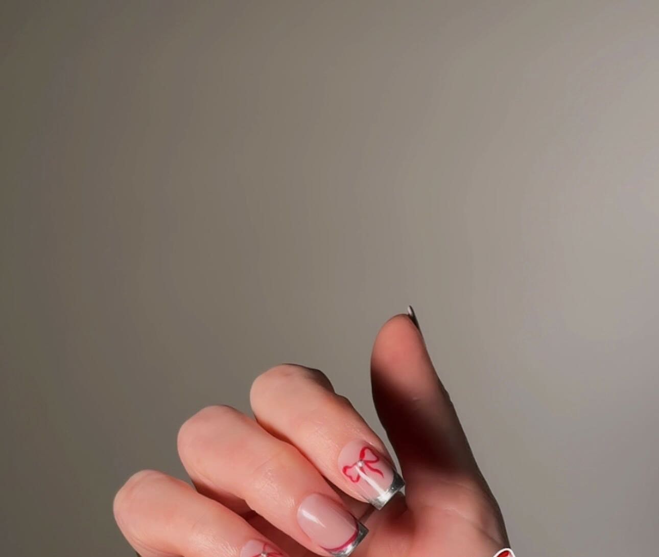 Dvije šake sa nude noktima i sitnim crvenim mašnicama kao nail art detaljem
