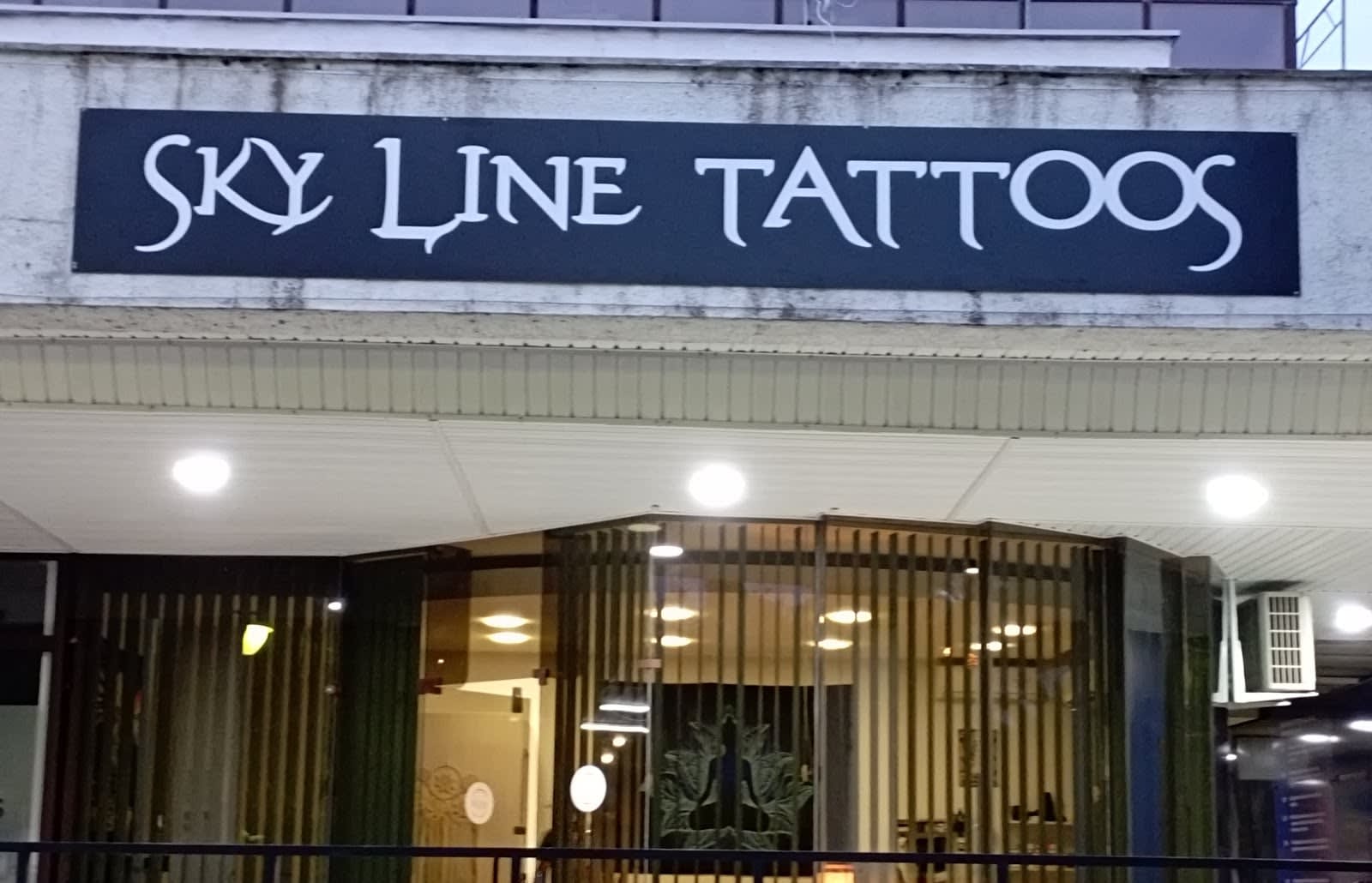 Ulaz u studio u sumrak: osvijetljen natpis Sky Line Tattoos iznad staklenih vrata kroz koja se nazire enterijer